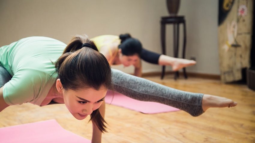 girl in green t-shirt and gray pants doing yoga on pink yoga mat
